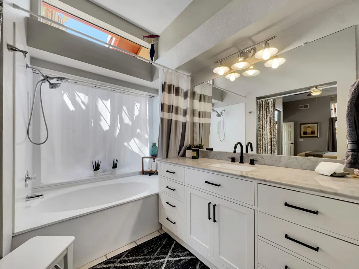 A spacious, stylish bathroom with a bathtub, double sink vanity, shower area, and a window letting in natural light. The clean, contemporary design conveys a spa-like ambiance.