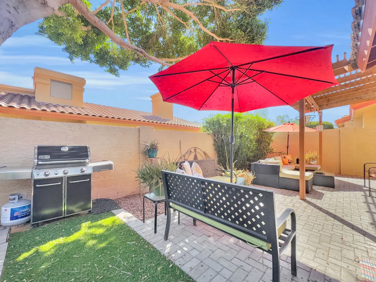 This exterior shot captures a relaxed barbecue scene with a grill, a red umbrella shading a cozy seating area, and lush greenery surrounding the space. The inviting setup is designed for outdoor dining, socializing, and enjoying meals under the open sky, perfectly echoing the section’s mention of evening barbecues and alfresco living.