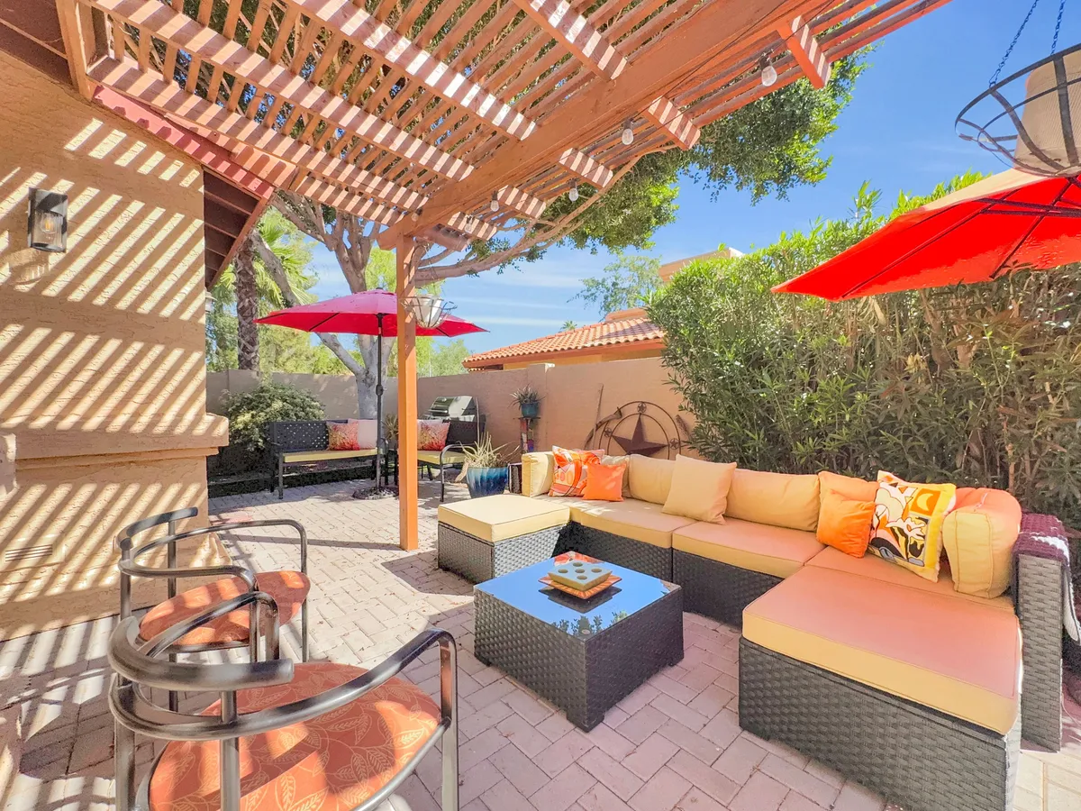 A cheerful outdoor lounge area featuring colorful umbrellas, plush decorative cushions, and a coffee table set up for entertaining. The space is well-suited for socializing, brunches, and unwinding outdoors, with a sunny and inviting ambiance.