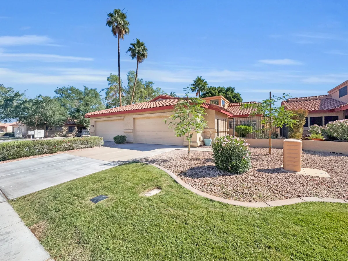 A tranquil backyard scene featuring a red tiled roof, towering palm trees, and meticulously maintained gardens. The setting is clearly designed for outdoor enjoyment, suggesting the comforts of a private, relaxing space at home.