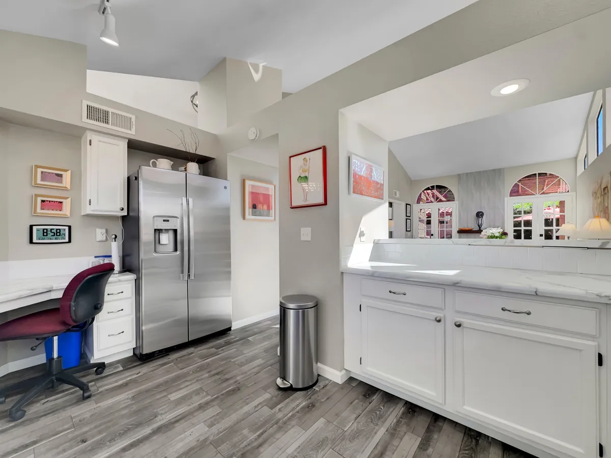 A contemporary kitchen with a stainless steel refrigerator, sleek white cabinets, eye-catching artwork, and an expansive kitchen counter. The setting is both inviting and modern, suggesting comfort and style for cooking and entertaining.