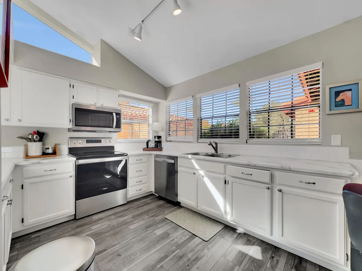 A cheerful kitchen scene highlighting modern kitchen appliances, a spacious sink, and large windows that flood the space with natural light. The counters are roomy, and the setup suggests an environment ideal for cooking, socializing, and family gatherings.