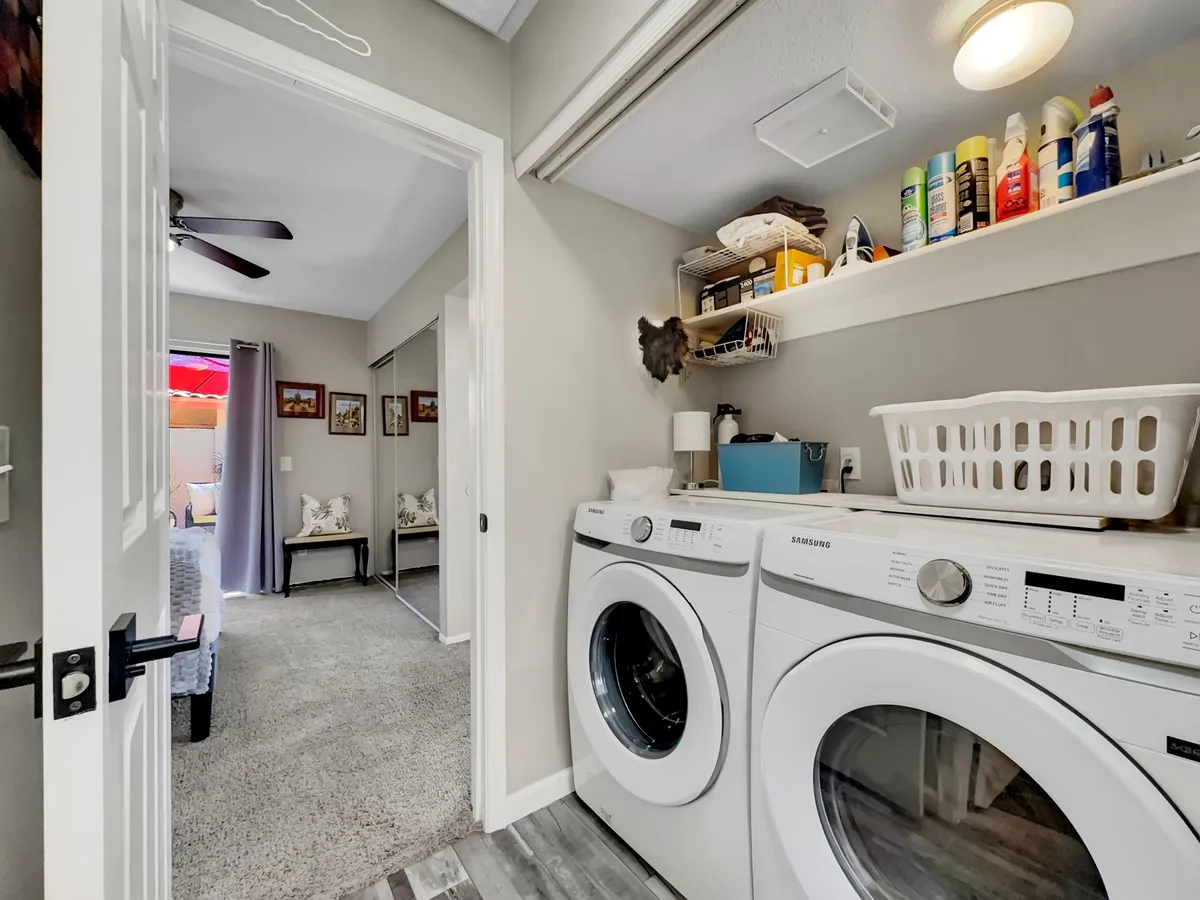 A tidy laundry area featuring a washing machine, dryer, shelves stocked with cleaning supplies, and a laundry basket. The space is organized and functional, supporting extended stays and the needs of busy guests.