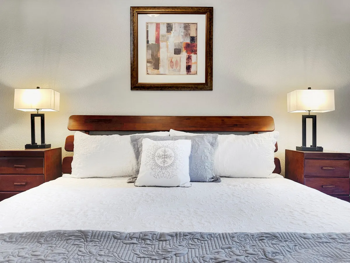 A relaxing bedroom with decorative pillows, framed artwork, and nightstands with lamps. The room has a cozy, inviting atmosphere, perfect for unwinding after a busy day.